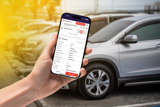 A contented person in a suit standing next to a red car in front of a view of the CarVerification website